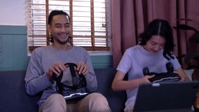 Young happy asian couple playing video games virtual reality glasses in living room. Cheerful people having fun with new trends technology. Man with hands up wearing the virtual reality goggles.