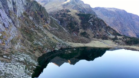 Lac d'Espingo reflecting mountain lake located in Haute-Garonne, Pyrénées, France, Aerial flyover pan right shot