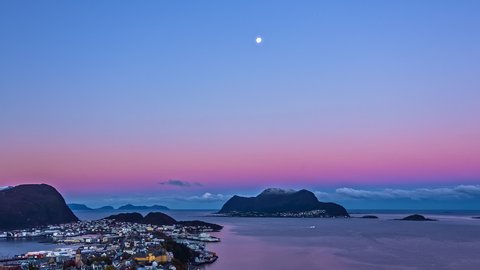 Aerial Time lapse of colorful dawn and sunrise over norwegian harbor city of Alesund at morning - Boat cruising on Geirangerfjord and clouds flying in background behind mountain range silhouette