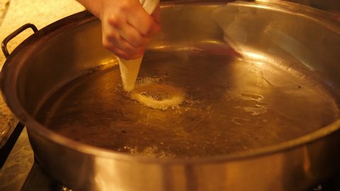 Close-up of the chef frying donuts in boiling oil, squeezing the dough out of the pastry bag into the oil.