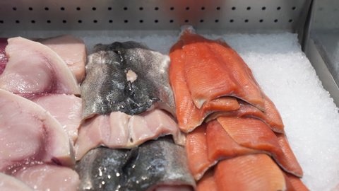 Various types of fish in seafood market display case, fresh raw fish fillets neatly stacked on ice in fishmongers shop case, dolly out HD
