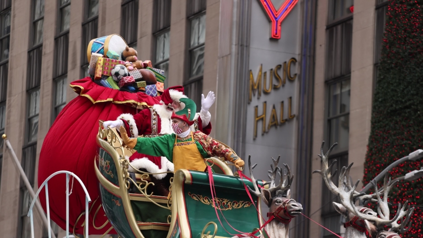 New York, USA - November 25, 2021: Santa Claus Sleigh with Christmas gifts from North Pole at Macy's Annual Thanksgiving Day Parade celebration near Radio City Music Hall in slow motion. Santa waives.