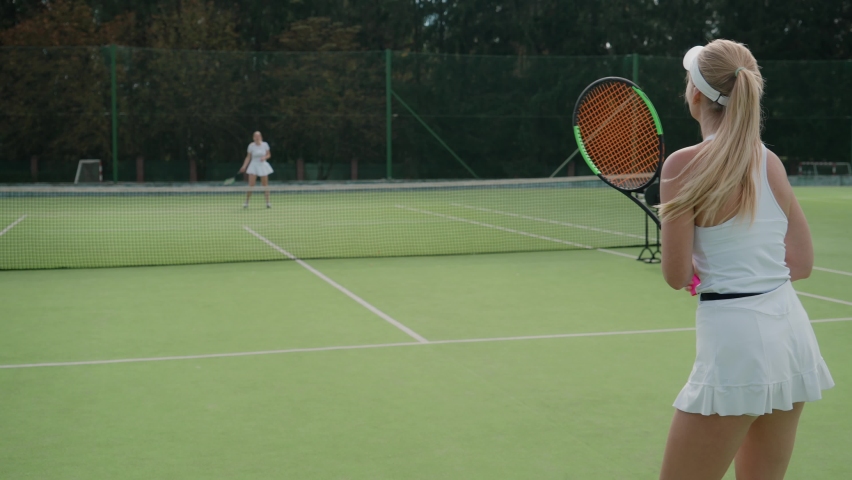 Back view of female tennis player hits the ball with a racket, female hits off the opponent's serves during tennis match, active game, 4k 50fps. Royalty-Free Stock Footage #1082946082
