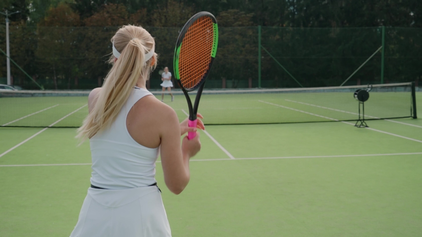 Back view of female tennis player hits the ball with a racket, female hits off the opponent's serves during tennis match, active game, 4k 50fps. | Shutterstock HD Video #1082946082