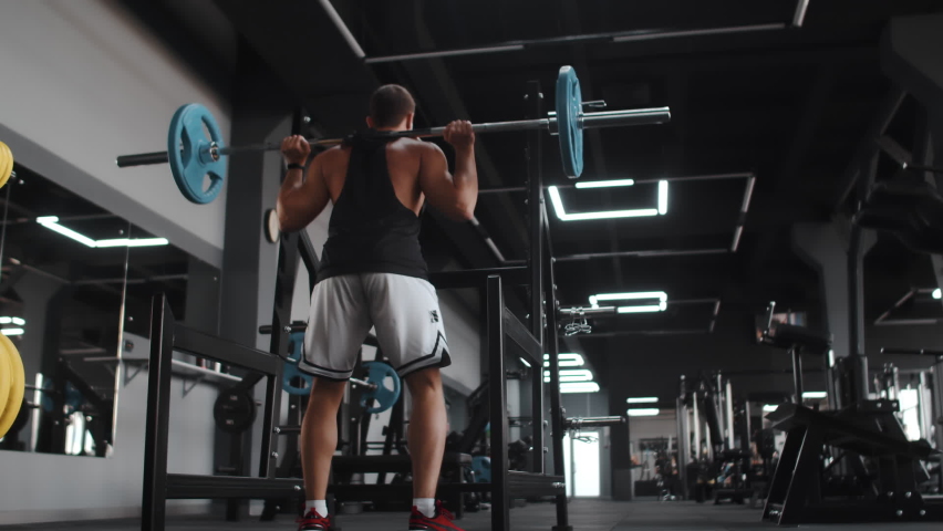 Muscular man training with barbell, doing squats in gym, back view. Bodybuilder trains in gym with barbell. Concept sports Royalty-Free Stock Footage #1082946280
