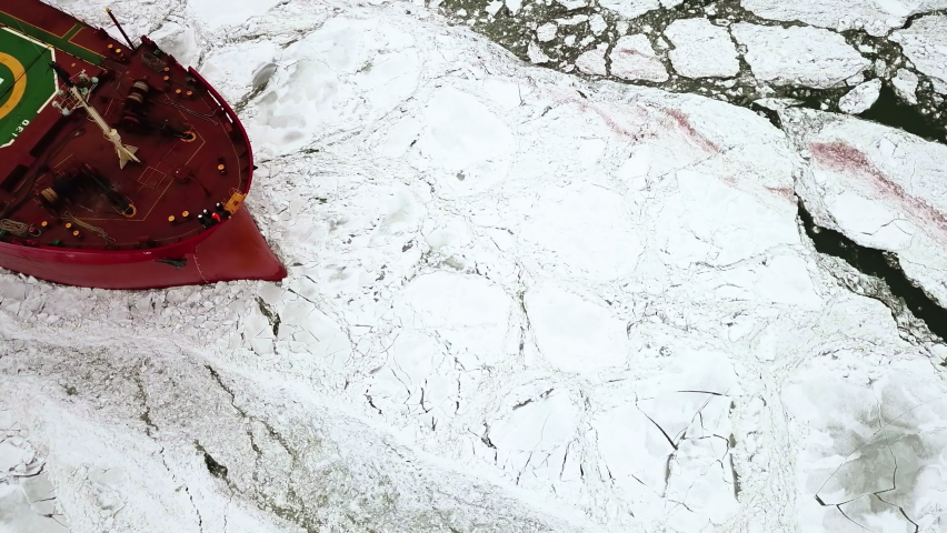 Drone top down Epic red steel icebreaker ship tanker breaks winter frozen sea, overcomes. Bow of ship floats through ice floe. Huge white block of ice.