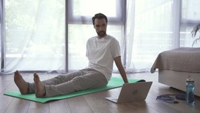 Man exercising on fitness mat near laptop in bedroom