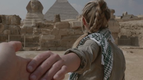 Slow motion: Follow me concept: Young woman holding companion hand, leading him towards the Great Pyramids of Giza. People travelling adventure concept. 