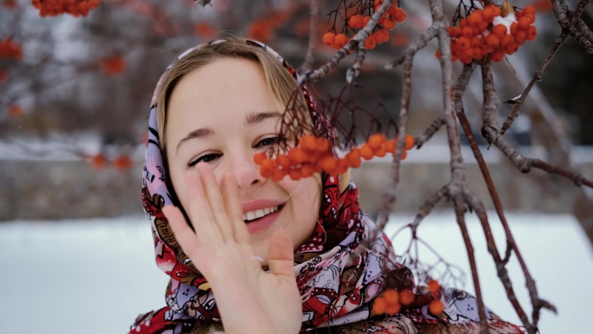 Portrait of a cute blonde near a bush with red rowan berries in a winter snow-covered park