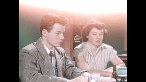 1950s: Teenagers sitting at table in restaurant, talking. Hands marking with clapperboard. Teen girl reading menu, looking around.