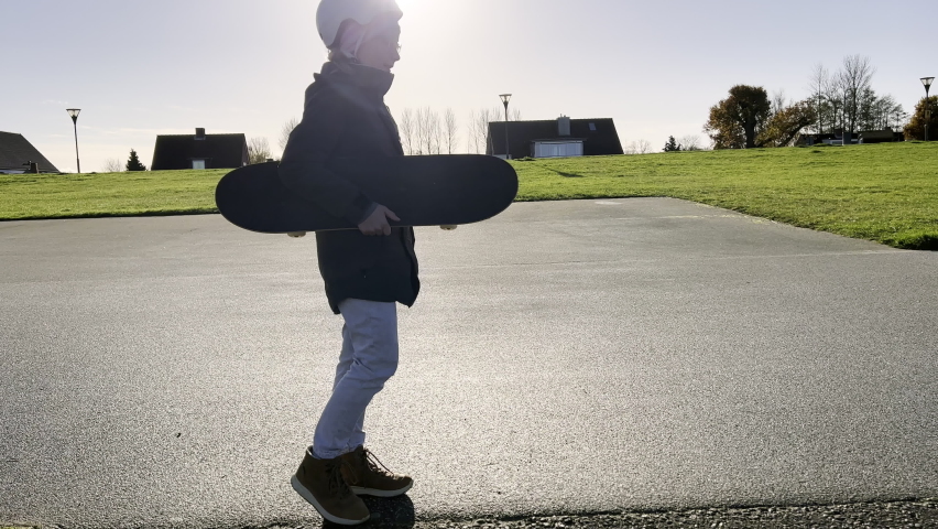Happy little girl in glasses with skatebosrd in hands walking. 4K 60FPS video