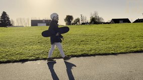 Happy little girl in glasses with skatebosrd in hands walking. 4K 60FPS video