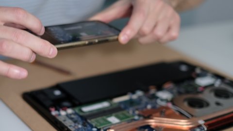 Unrecognizable engineer takes pictures of the laptop motherboard on a smartphone. Electronic renovation, business, occupation concept