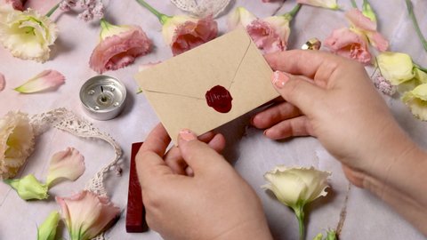 Hands put wax sealed envelope on a marble table near pink flowers close up 