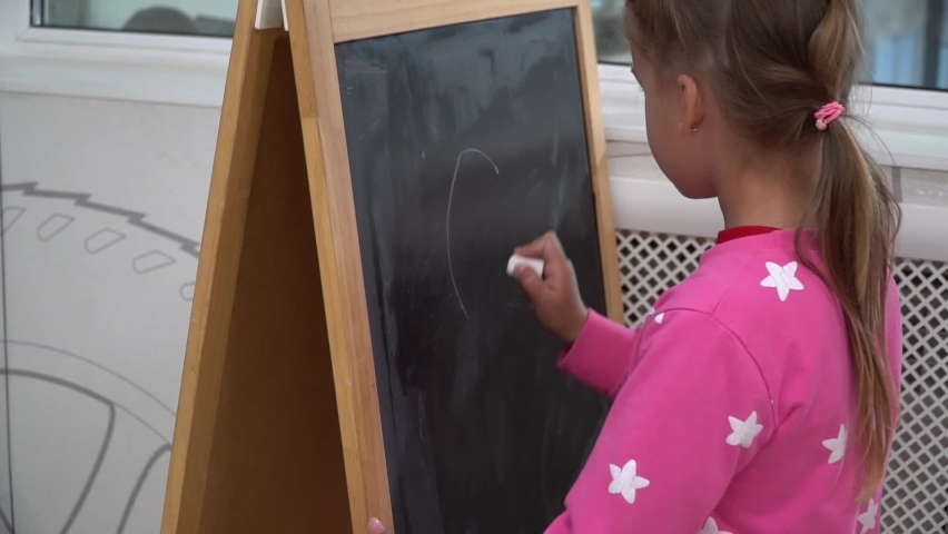 Girl draws circles with chalk on a blackboard