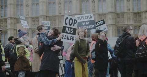 London, UK - 11 20 2021: Young activist couple hugging on Bridge Street in Westminster holding signs, ‘Cop Has Failed’ and ‘Betrayed By My Government’, for an Insulate Britain protest.