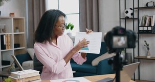 Cute positive confident skilled african american woman sitting in front of camera during video chat with client and explaining report with chart,distant work concept