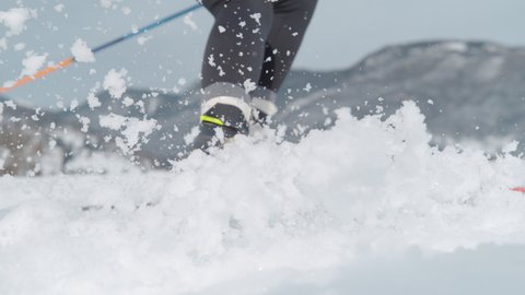 SLOW MOTION, LOW ANGLE, CLOSE UP, DOF: Female skier turns hard and sprays wet snow at camera. Woman is spraying snow with her skis during a skiing training session in Slovenian mountains