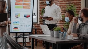 Man and woman with face mask planning business growth in front of coworkers at briefing meeting. Colleagues using monitor to do financial presentation for marketing strategy during pandemic. - Powered by Shutterstock - Get 15% off with code: PIKWIZARD15