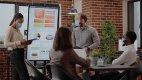 Multi ethnic colleagues doing business presentation in office. Man and woman with face mask talking to workmates about project planning and marketing strategy during covid 19 pandemic. - Powered by Shutterstock - Get 15% off with code: PIKWIZARD15