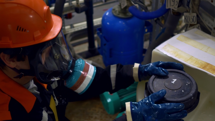A worker in the chemical industry in a helmet and a gas mask unscrews a container with pesticides. Work in conditions of contamination or poisonous substances Work in hazardous production and industry Royalty-Free Stock Footage #1082986801