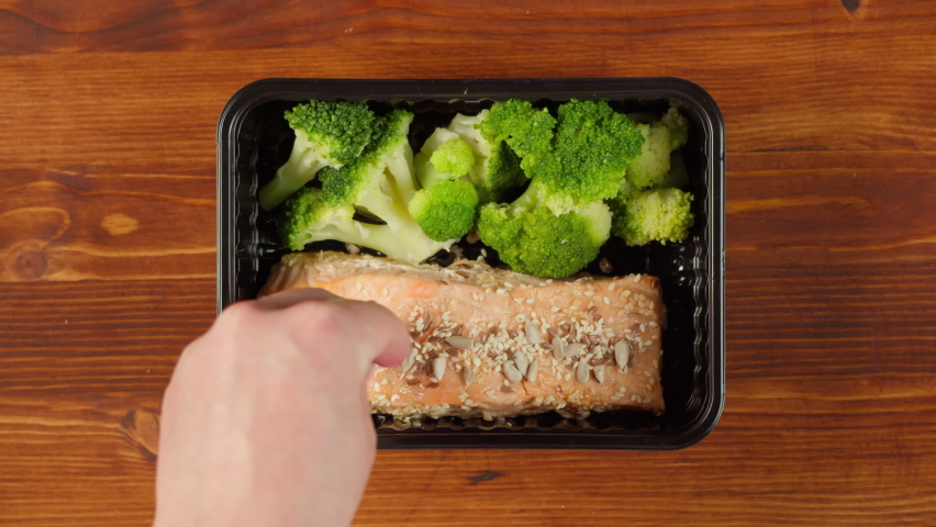 Salmon steak and broccoli close-up. Food delivery top view, take away meal in disposable container on wooden table. Lunch box with cooked vegetarian dish. Healthy diet. Catering service concept.