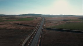 Aerial of an asphalt road located between two land areas while a van and car drive through it. Drone view of sunny day during autumn.