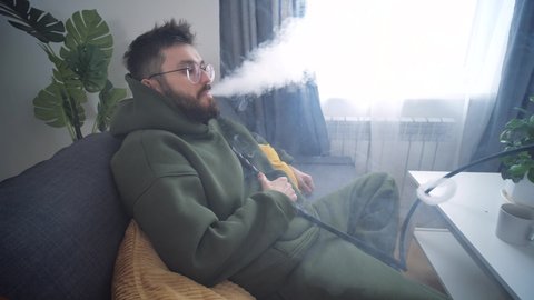 Rest and relaxation concept. Man smokes a hookah in room of home interior