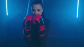 Beautiful woman kickboxer beats with fists in boxing gloves towards the camera, dodging punches. POV-shot through the eyes of an opponent. Aggressive angry woman boxing professionally in a dark gym - Powered by Shutterstock - Get 15% off with code: PIKWIZARD15