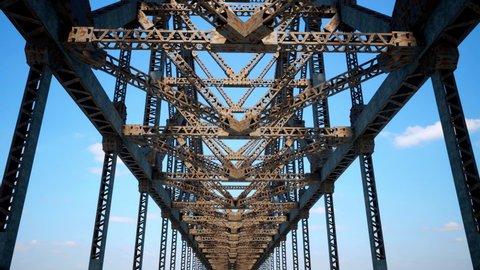 Looking up at an old and rusty steel-structured truss and girder bridge as the camera passes directly below.