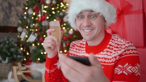 Man communicates video with friends and family via video call. Congratulations on social networks. New Year 2022. Man sits near Christmas tree with gifts. Person with glass of champagne, sweater deers