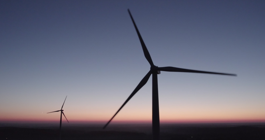 AERIAL VIEW: two rotating silhouettes of wind turbine propellers against the night sky. Eco-friendly generation of electricity from wind energy. Concept of renewable energy sources. Royalty-Free Stock Footage #1083001018