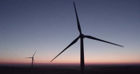 AERIAL VIEW: two rotating silhouettes of wind turbine propellers against the night sky. Eco-friendly generation of electricity from wind energy. Concept of renewable energy sources.