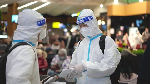 Moscow, 13.11.21: Chinese passengers or tourists at airport terminal in Covid-19 uniforms. Facemasks and face shields, airplane coronavirus restrictions. Medics in covid 19 suits wait plane boarding.