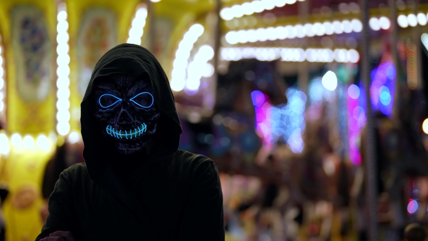 Portrait of a woman in a death mask glowing with neon fire on the background of an amusement park | Shutterstock HD Video #1083001435