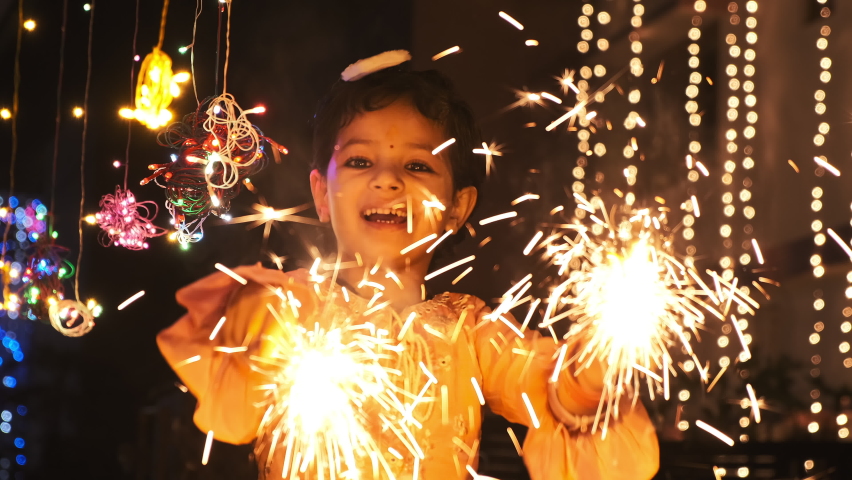 Shot of a beautiful little Girl Celebrating Diwali Festival in India. An Indian young girl playing with fire crackers and looking into camera with beautiful smile. A festival of light in India. Royalty-Free Stock Footage #1083002758
