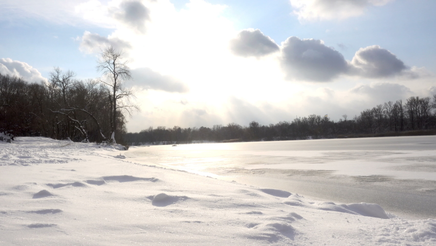 Winter landscape in time laps of a frozen river with a snow-covered bank and clouds. 