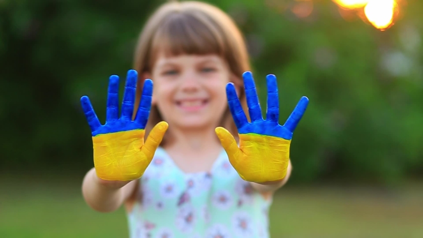 Joyful child girl waving hands painted in Ukraine flag colors and say hello outdoor at nature background, focus on hands Royalty-Free Stock Footage #1083006934