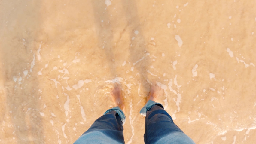 Sea waves washing over male feet, Young Indian man standing on seashore and enjoying tides of sea on trip, Guy enjoying summer vacation at seaside. Top View POV At Shivrajpur beach in Gujarat, India