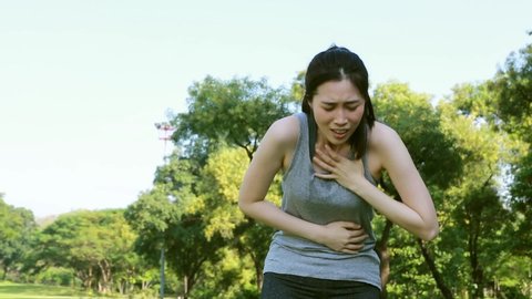 Woman exercising outdoors has chest pain, acute heart attack : Young woman suffering from heart disease holds her chest in agony.