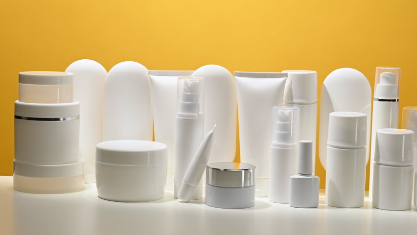 jar, bottle and empty white plastic tubes for cosmetics on a yellow background. Packaging for cream, gel, serum, advertising and product promotion Royalty-Free Stock Footage #1083011308