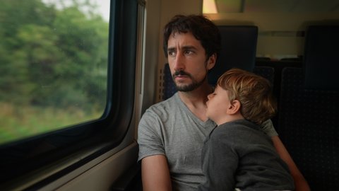Father traveling by train with sleeping toddler son. Child on dad lap asleep