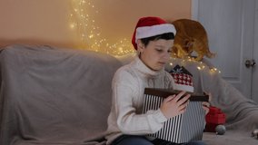Portrait of a boy wearing a Santa hat. Boy opens the box. Present. The emotion of surprise and happiness. Christmas. 4K