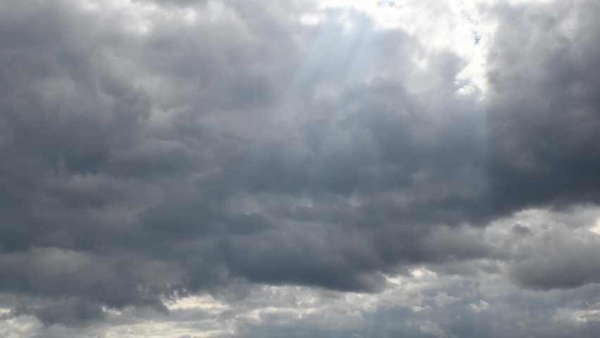 Time lapse sunbeams break through grey cumulus clouds in sky. Cumulus cloud cloudscape timelapse. Weather change from stormy clouds to white fluffy clouds in clear blue sky. Skyscape background