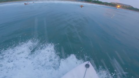 Point of view of a surfer starting from a wave and driving past another rowing server and showing him a shaka gesture. Surfer ride with friends at sunset and beach. Dynamic surfing.
