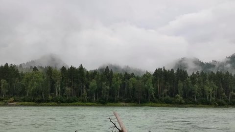 Stunning fog over calm river and forest hills, cloudy sky. Early misty morning in mountains. Beautiful natural background.