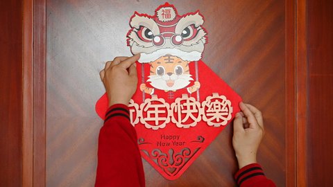man sticking a Chinese New Year of tiger 2022 mascot to the door no logo no trademark translation of the Chinese is happy new year