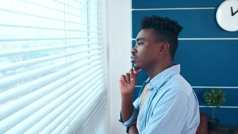 Young thoughtful African American business man entrepreneur looking out window planning ahead thinking of ideas for future business development. Pensive manager pondering of problem solution at office