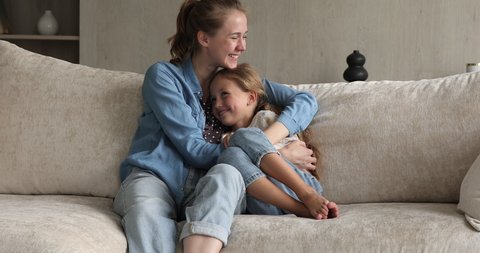 True love and devotion. Loving family of two foster mother and preteen adopted daughter cuddle on sofa at living room. Caring elder sister spend time with younger one talk feel emotional bonding laugh