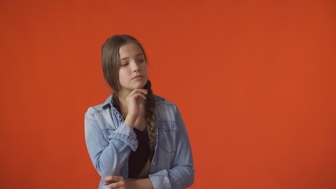 A young girl looks thoughtfully up in an orange background. Copy space. 